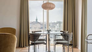 En matplats med ett runt bord och stolar, en hängande lampa och utsikt över en stadssiluett genom stora fönster.