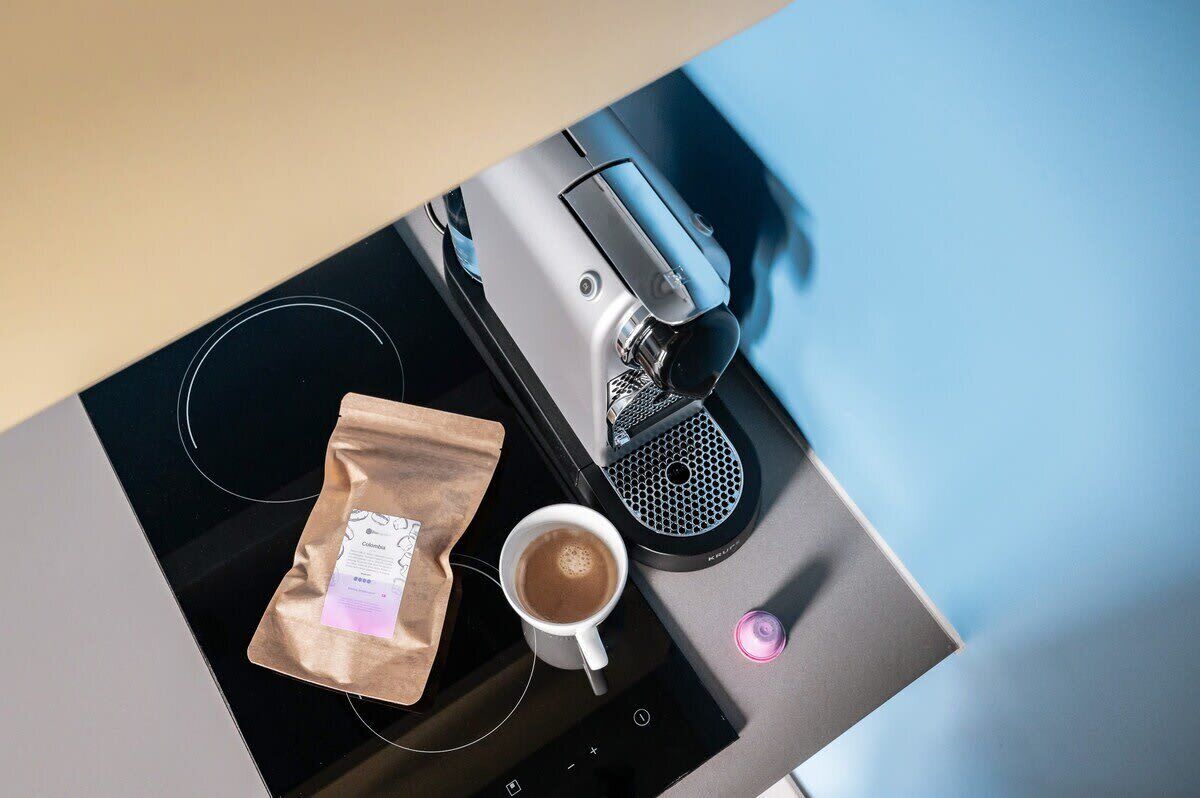 En kaffemaskine med en kop kaffe og en kaffepose på en bordplade.