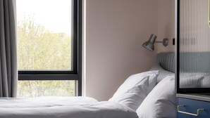 A neatly made bed with white linens, a bedside lamp, and a view of trees through a window. - Århus North Studio Apartment by Daniel&Jacob's (Aarhus)