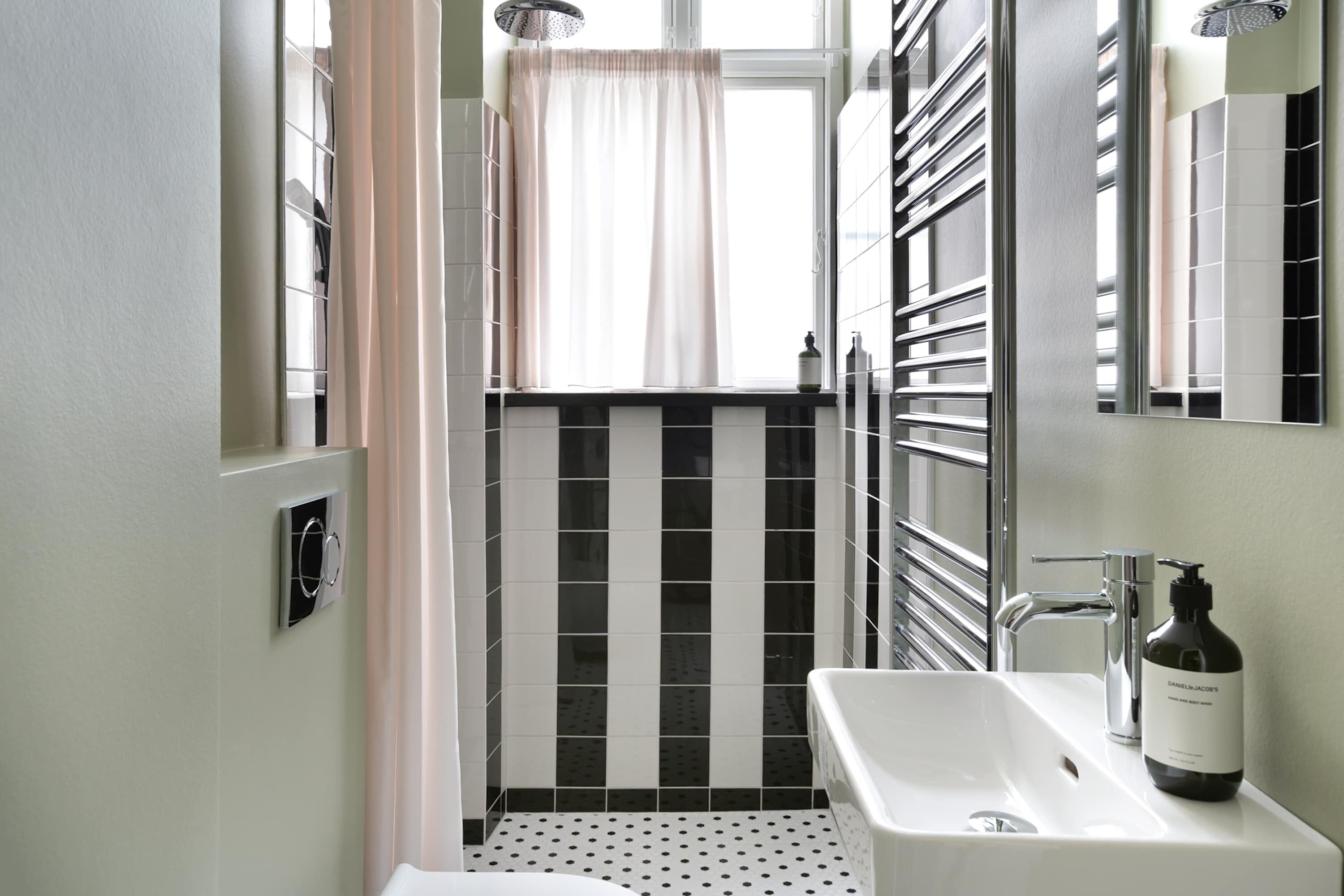 Une salle de bain avec un lavabo blanc, un miroir, une douche avec un rideau et un radiateur.