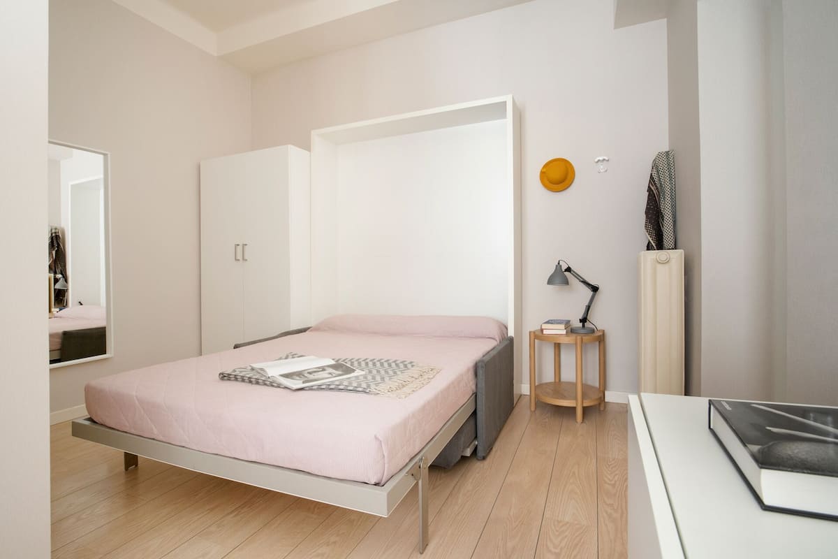Um quarto moderno com uma cama, uma mesa de cabeceira com abajur, um espelho e um radiador.