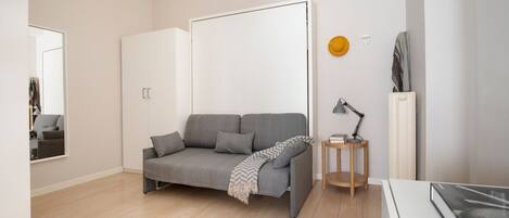 A modern living room with a grey sofa, a small wooden side table, a floor lamp, and a radiator.