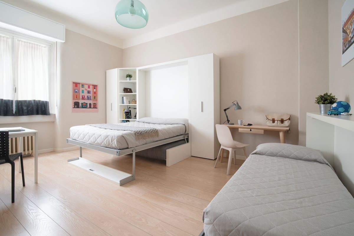 Quarto moderno com cama, escrivaninha, cadeira e unidade de armazenamento.
