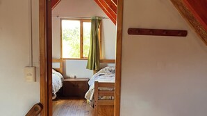 A bedroom with a wooden bed, a window with a curtain, and a wooden floor. - Ca bañas Giardino in Lago Ranco (Lago Ranco, Los Ríos)