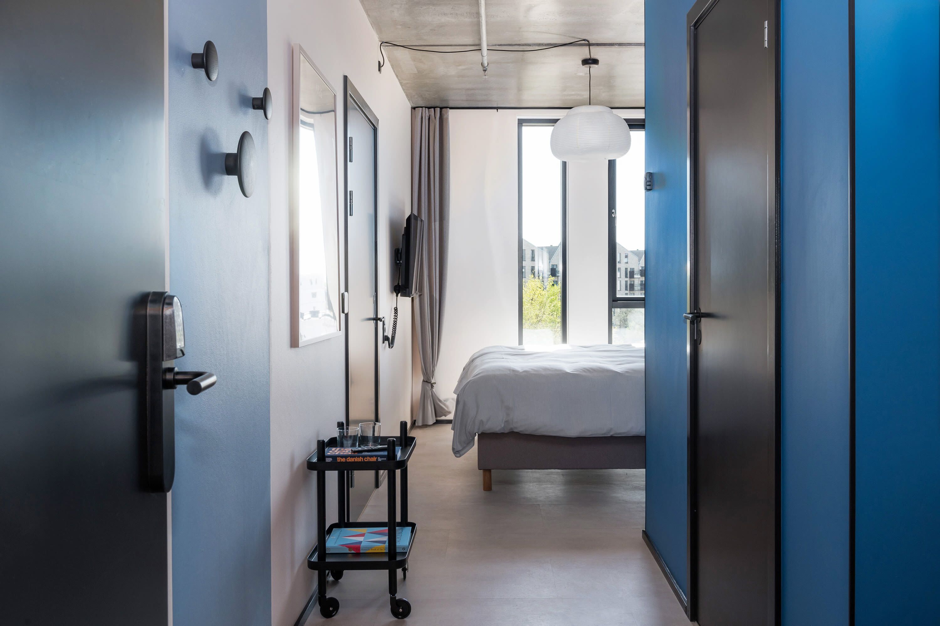 Ein modernes Hotelzimmer mit einem großen Bett, einem Schreibtisch mit Stuhl, einem Fernseher und einem Fenster mit Blick auf Gebäude.