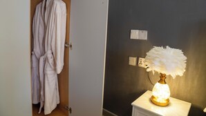 A bathroom with a white robe hanging on a rack, a white lamp with a feathered shade, and a light switch on the wall.