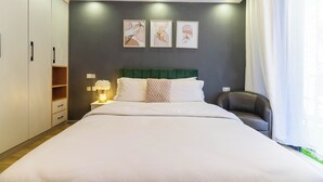 A bedroom with a bed, a green headboard, a nightstand with a lamp, a chair, and a window with curtains.