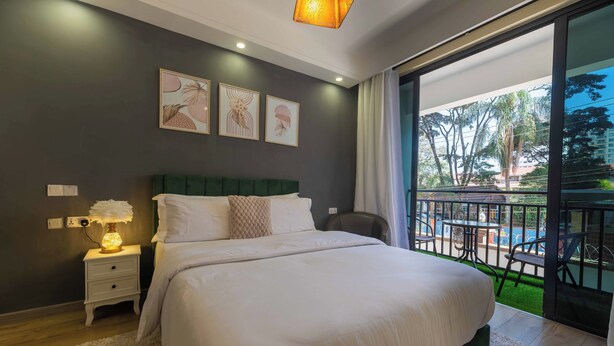 A bedroom with a large bed, a nightstand with a lamp, a green headboard, and a view of an outdoor balcony with a table and chairs.