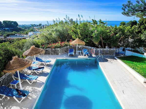 A swimming pool with lounge chairs and a thatched umbrella, surrounded by greenery and a view of the sea. - Vacation home Monet by Interhome (Nerja)