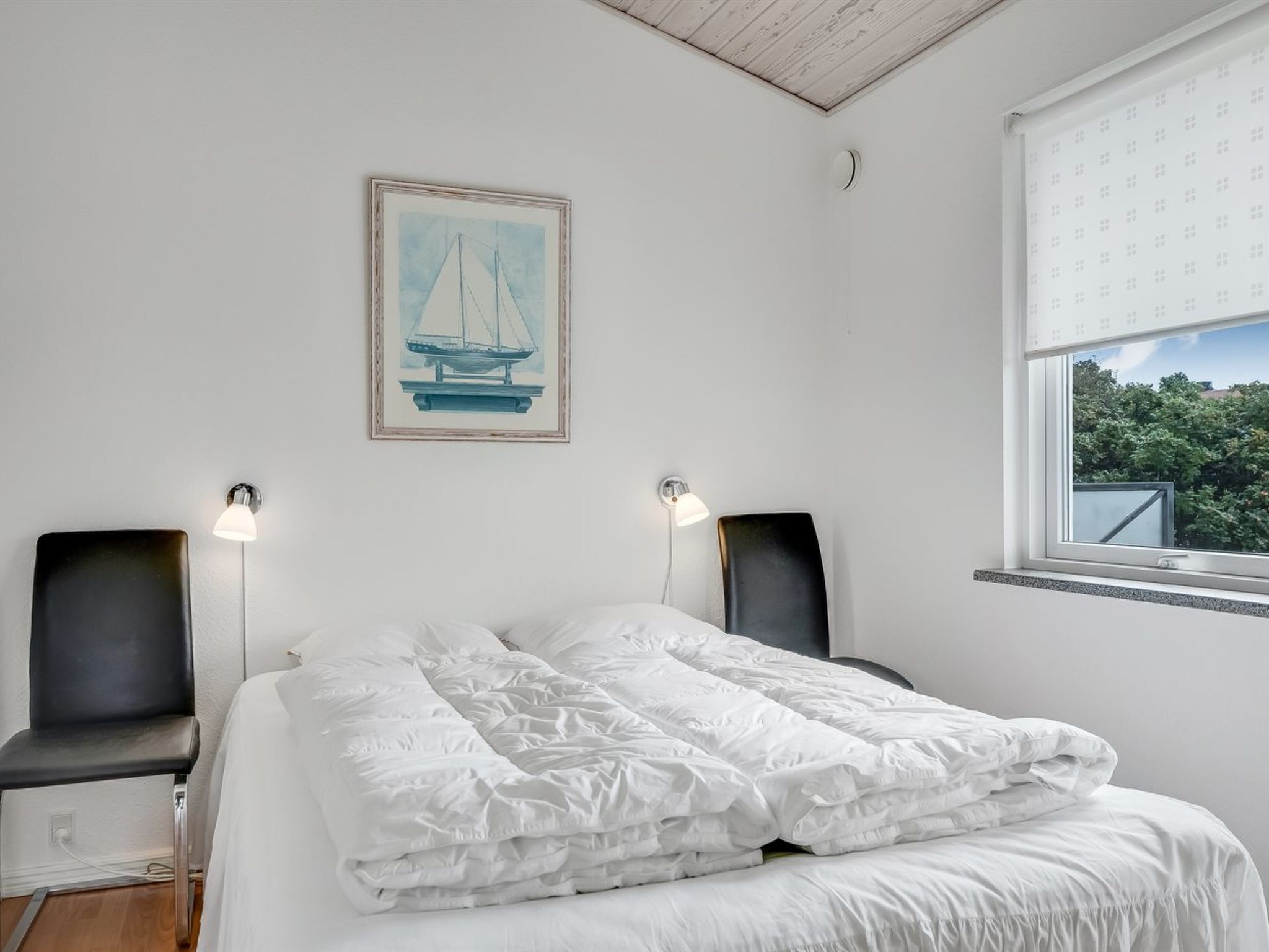 A bedroom with a bed, two chairs, a painting, and a window with a view.