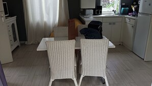 A compact kitchen with white cabinetry, a dining table with wicker chairs, and a window with curtains.