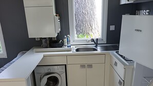 A compact kitchen with a built-in washing machine, a sink, and a window with a view of trees.