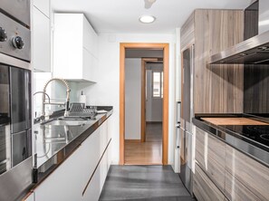 Eine moderne Küche mit Edelstahlgeräten, einer Holztür und Blick in den angrenzenden Raum.