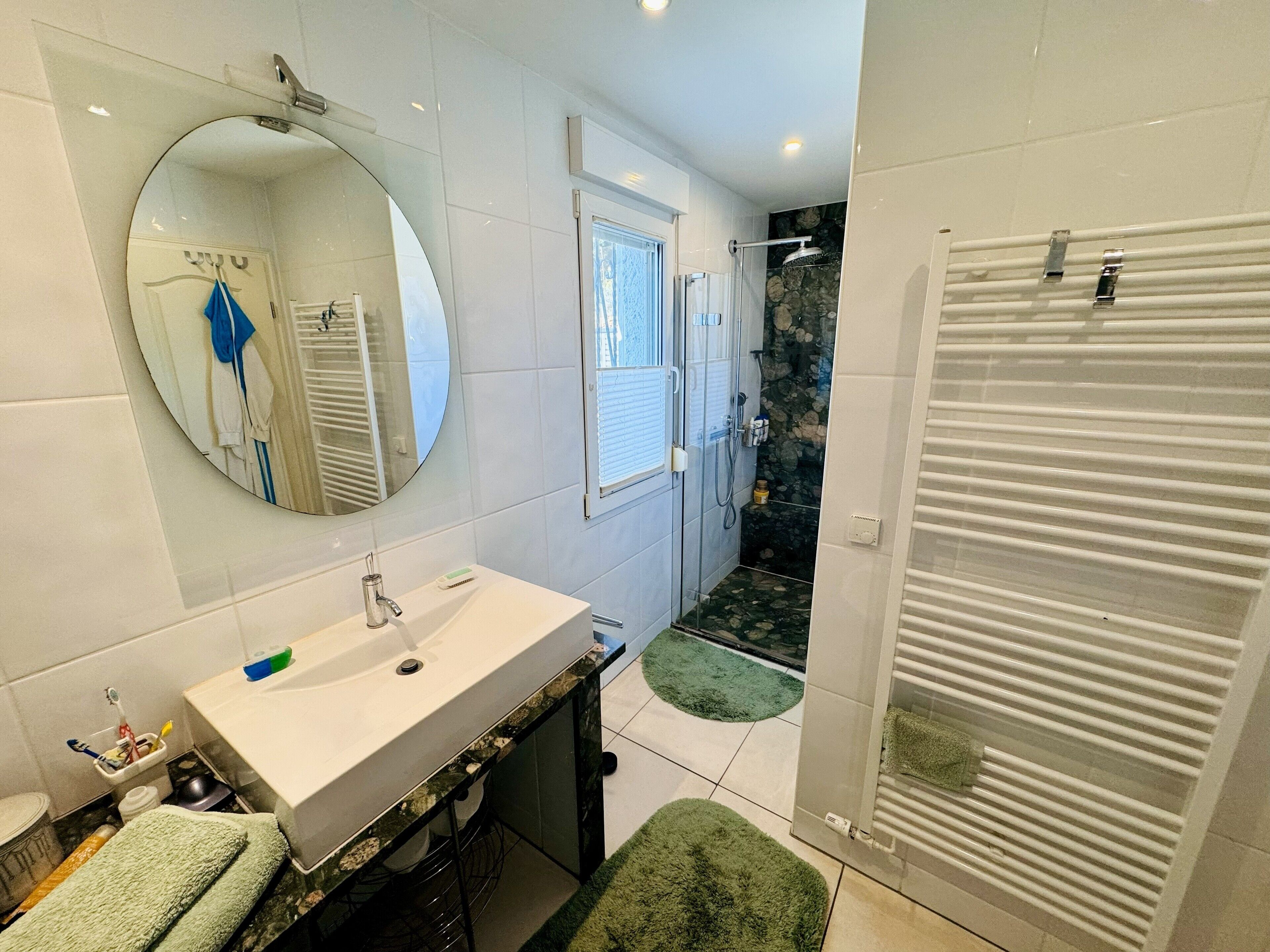 Een moderne badkamer met een grote spiegel, een wit wastafelmeubel en een douchehoek.