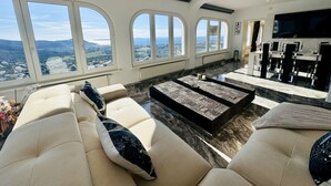 A spacious living area with a large window overlooking a scenic landscape, a comfortable seating area, and a modern entertainment setup. - Villa Serenity | Private pool, air conditioning, view of the bay of Roses, up to 13 people (El Mas Fumats)