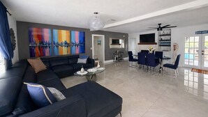 A modern living room with a sectional sofa, a dining area with a TV, and a large abstract painting on the wall.