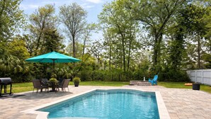 A rectangular swimming pool with a tiled deck, surrounded by a landscaped garden and a wooden fence.