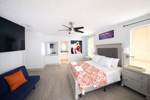 A modern hotel room with a bed, a ceiling fan, a bathroom visible through an open door, and a TV mounted on the wall.