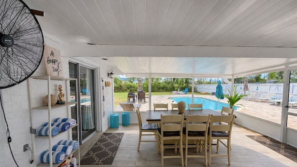 A covered patio with a pool, wooden furniture, and a fan.