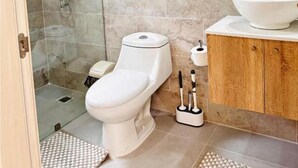 Un baño con inodoro, bidé y ducha. Hay un lavabo con una pileta y un espejo encima.