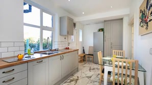 Une cuisine moderne avec des meubles blancs, un plan de travail en bois, un évier et un coin repas comprenant une table et des chaises en verre.
