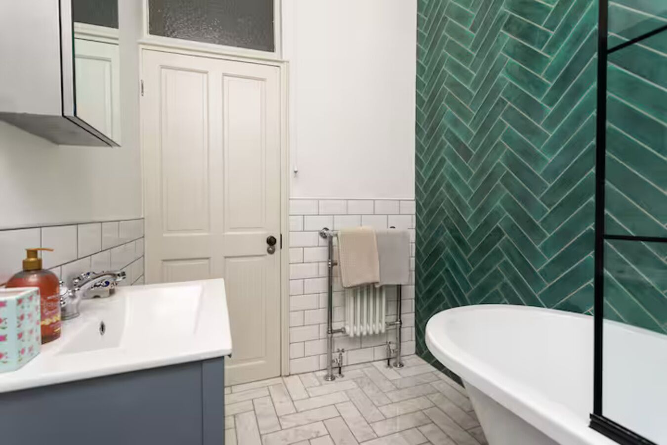 Ein Badezimmer mit einem weißen Waschbecken, einer weißen Badewanne, einem Handtuchhalter und einer Heizung.