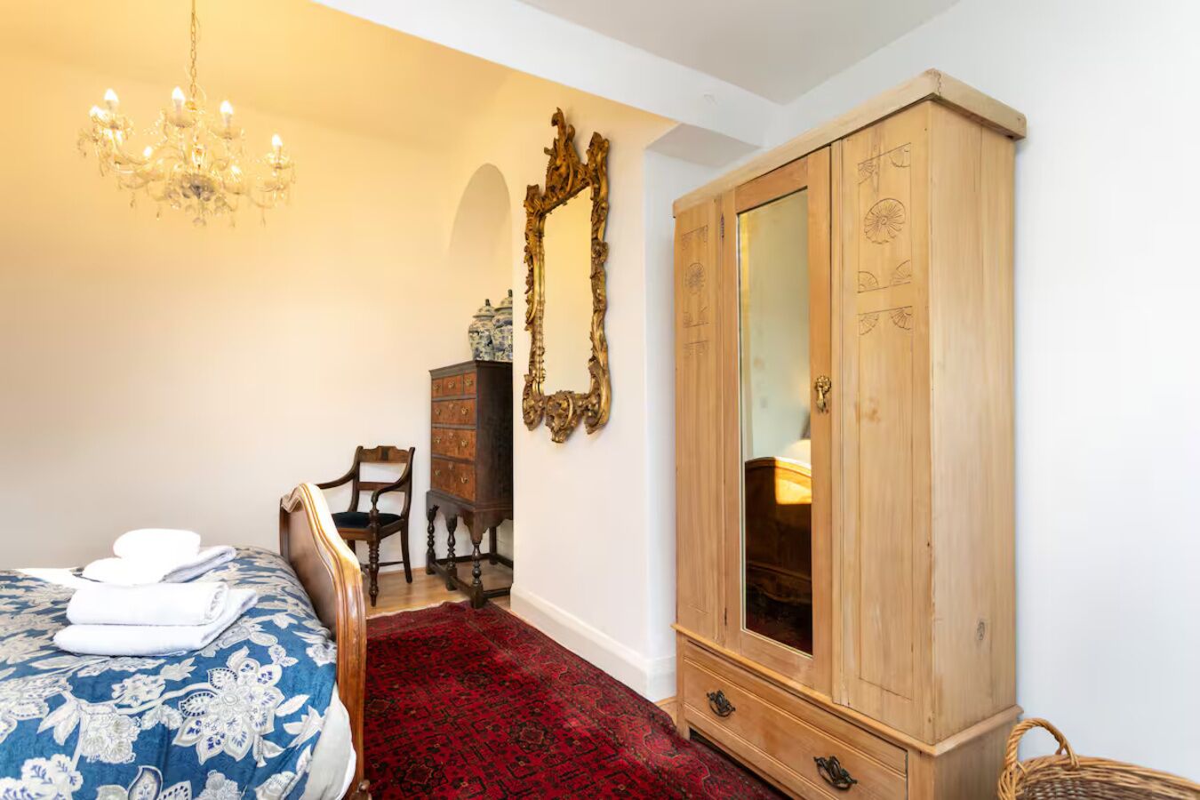 Un dormitorio con cama, armario de madera, silla, espejo y candelabro.