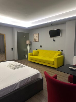 Een hotelkamer met een bed, een felgele bank, een rode stoel, een tafeltje, een televisie en een lamp.