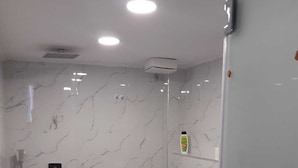 Une salle de bain moderne avec des toilettes blanches, une douche et un mur décoré d’un motif imitant le marbre.