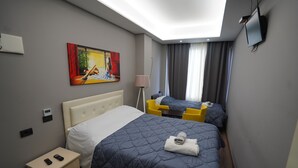 Une chambre d’hôtel avec deux lits, un tableau au mur, une télévision et une table de chevet avec une lampe.