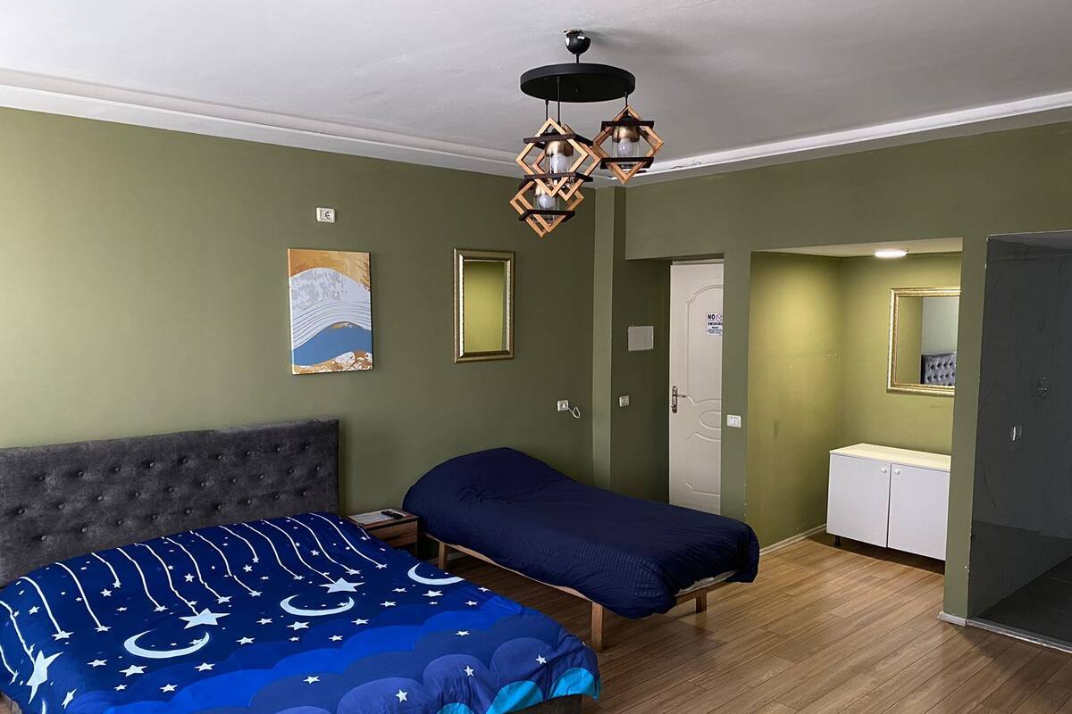 Une pièce comprenant un grand lit, un plus petit lit, une armoire, un miroir et une porte.