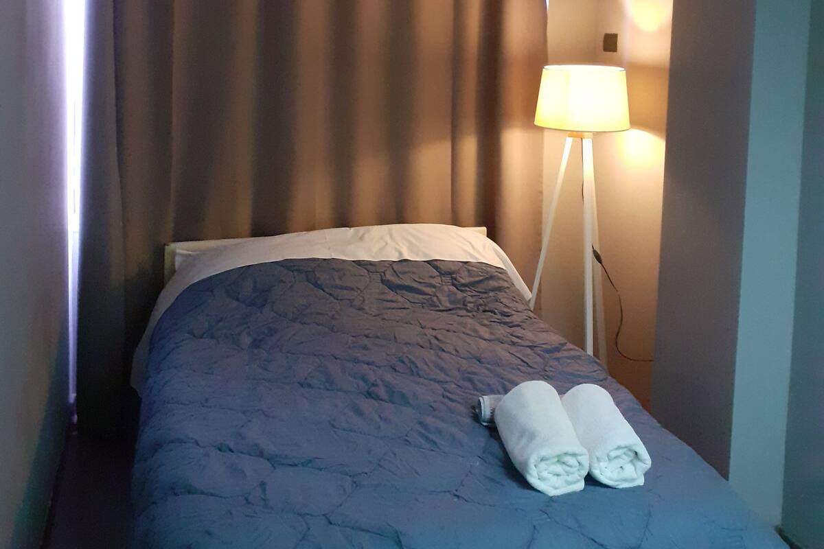 Une chambre d’hôtel avec un lit, une table de chevet, une lampe et une fenêtre avec des rideaux.