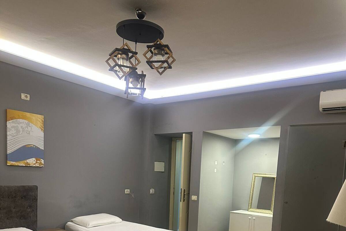 Une chambre d’hôtel avec deux lits, une table ronde, un miroir et un luminaire au plafond.