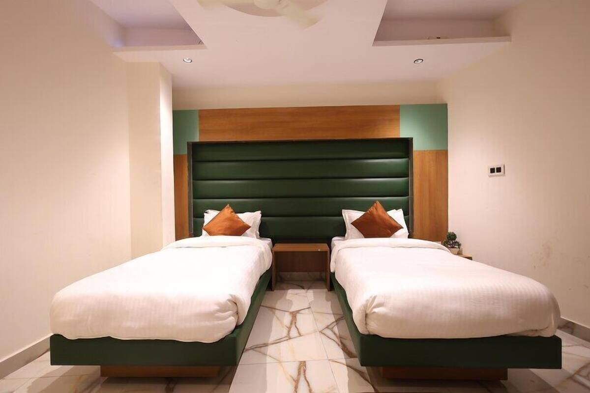 Une chambre d’hôtel avec deux lits simples, une tête de lit verte et un sol à motifs de marbre.