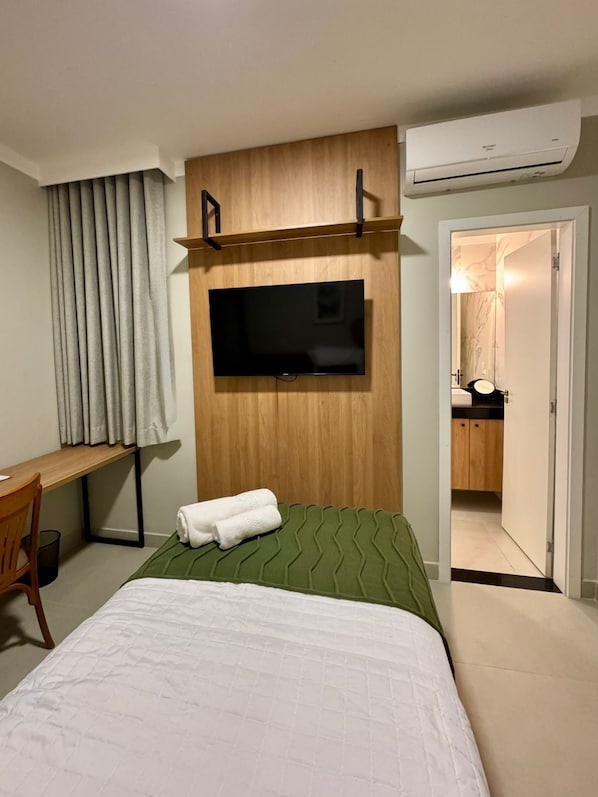A hotel room with a bed, a TV mounted on the wall, a desk, and an air conditioning unit. - Gran Amazon Av. Júlio César (Belém)