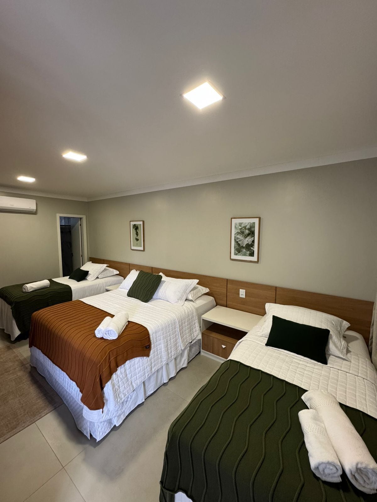 Habitación de hotel con dos camas, una mesita de noche y aire acondicionado instalado en la pared.