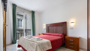 Ein Schlafzimmer mit Bett, Nachttisch, Holz-Kopfteil, Fenster mit Vorhängen und einer Wandlampe.