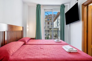 A hotel room with a bed, a TV, a window with curtains, and a view of buildings. - Room 'Habitación 204 Triple' with Balcony, Wi-Fi and Air Conditioning (Granada)