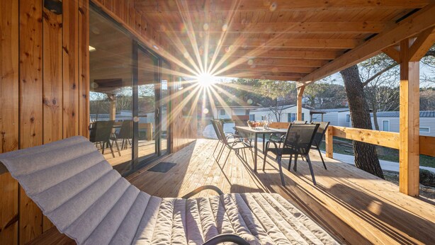 A sunlit wooden deck with a lounge chair and table, overlooking a residential area. - Camping Karin - Mobile houses Magoro (Donji Karin)