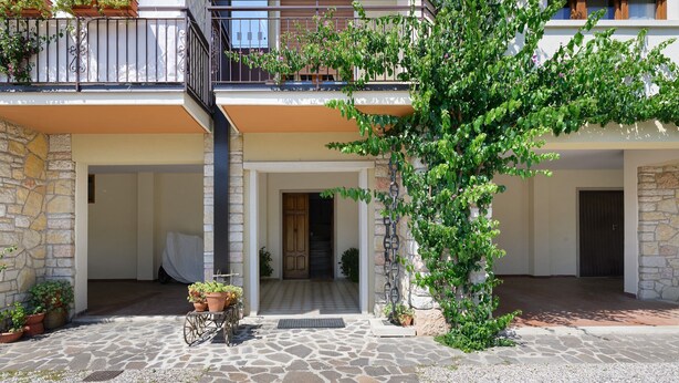 Un bâtiment doté d’une façade en pierre, d’un balcon avec des balustrades en métal et d’un arbre aux feuilles vertes.