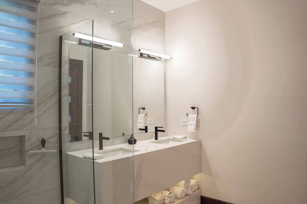 Een moderne badkamer met een douchecabine van glas, een marmeren werkblad en een grote spiegel.