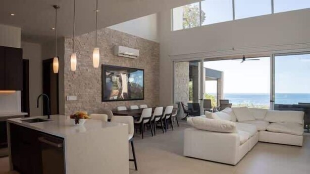 Una sala de estar moderna con un sofá blanco grande, un comedor con sillas y una cocina con una isla central.