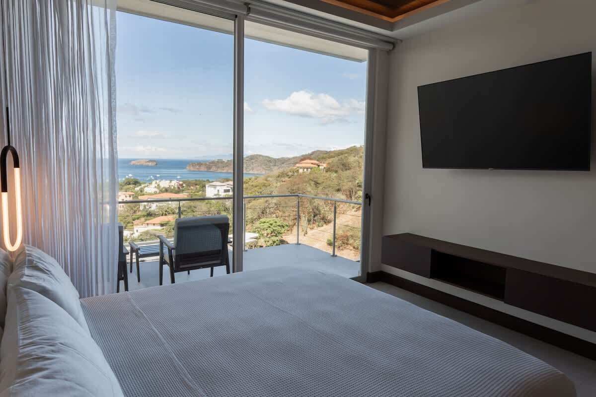 Una camera da letto con un letto grande, una TV montata a parete e un balcone vista mare e colline.