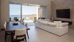 Una sala de estar moderna con un sofá grande, una mesa de comedor y un televisor montado en la pared.