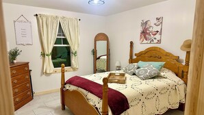 Un dormitorio con cama de madera, tocador, espejo y ventana con cortinas.