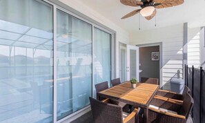 A modern room with a large sliding glass door, a wooden dining table with wicker chairs, and a ceiling fan. - 5BR Resort Home with Private Pool (Davenport)