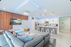 Ein modernes Wohnzimmer mit grauem Sofa, einem kleinen Couchtisch und einer farbenfrohen Kinderspielecke.