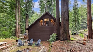 A cabin with a sloped roof, wooden deck, and Adirondack chairs.