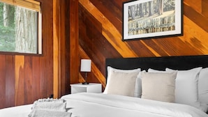 A bedroom with a wooden wall, a bed with white bedding, a nightstand with a lamp, and a framed picture on the wall.