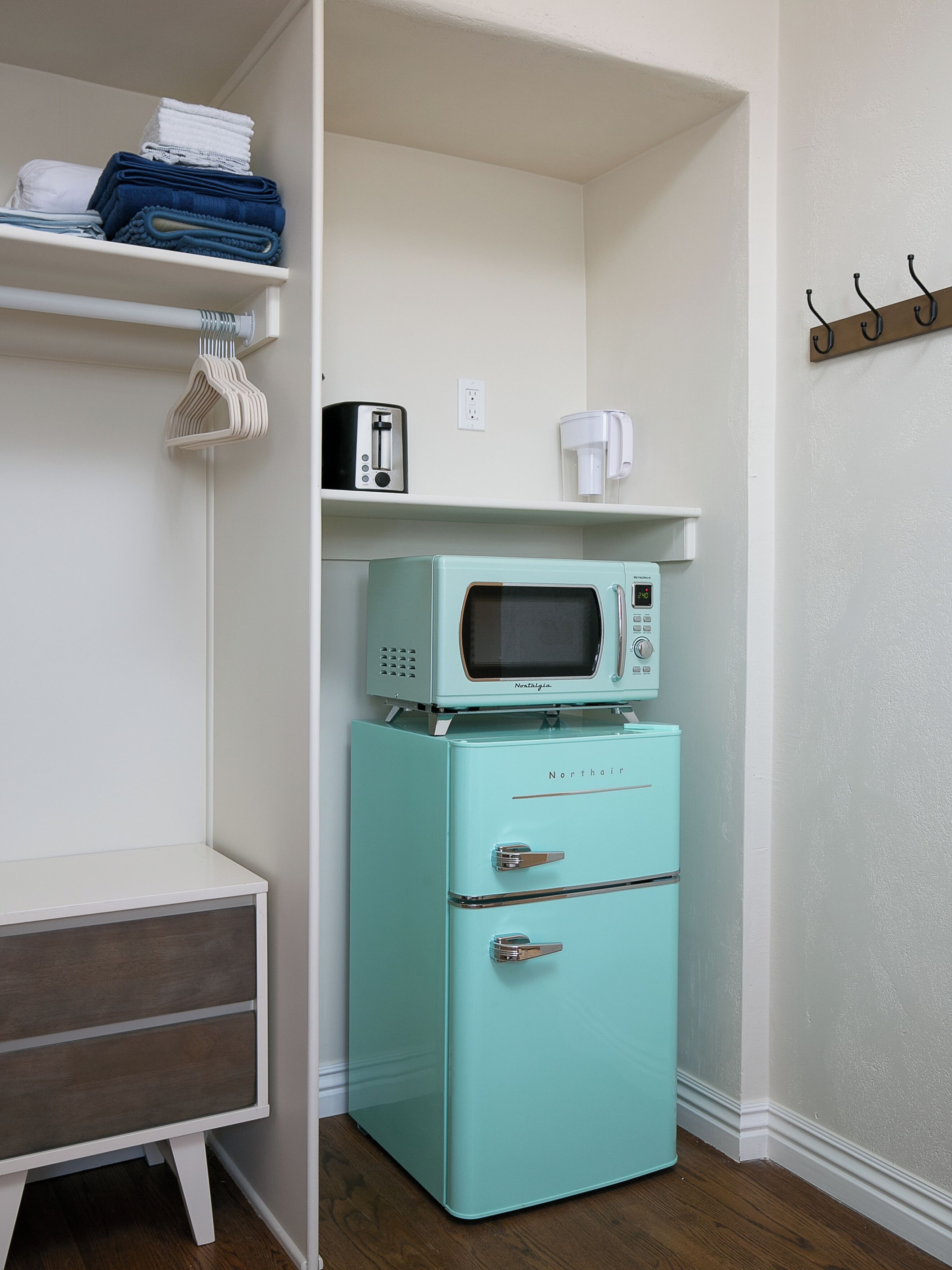 A compact kitchen with a vintage-style refrigerator and microwave, a small coffee maker, and a shelf with folded towels.